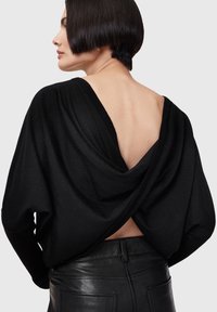 Black draped sweater with an open back, featuring soft fabric, a relaxed fit, and long sleeves, paired with sleek black leather pants.