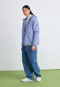 Ljust blå lättviktig jacka med huva, sidfickor och manschetter, tillsammans med lösa denimjeans och vita sneakers.