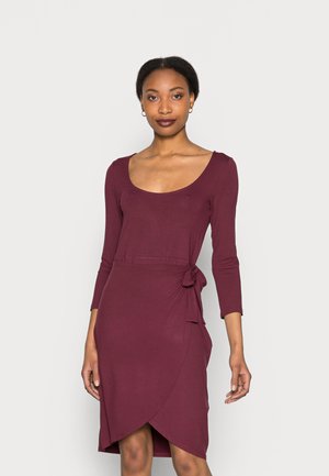 Vestido justo em malva com decote redondo, mangas 3/4 e detalhe de amarração lateral. O tecido tem uma textura suave e um design envolvente até ao joelho.