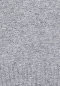 Gros plan sur un tissu tricoté doux et gris clair avec une texture fine et un motif côtelé sur le bord inférieur.