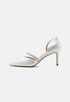 Ασημί γόβα με μυτερή μύτη, χαμηλό τακούνι στιλέτο και λεπτό λουράκι διακοσμημένο με στρας στο πάνω μέρος του ποδιού.