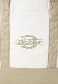 Kanvas totebag med beige stropper, kremfarget kropp og trykt lysebrun logo. Har en frontlomme og forsterkede sømmer.