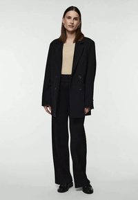 Black double-breasted tailored blazer over a beige top, paired with black ribbed wide-leg pants and black loafers. Smooth texture, structured design.