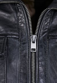 Zwarte leren jas met een opvallende zilveren rits, gestructureerde afwerking en contrasterende stiksels langs de randen.