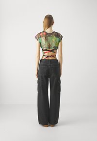 Avarustav roheline mesh crop top mitmevärviliste mustritega, kombineeritud mustade laiade cargo pükstega, millel on küljetaskud ja kõrge vöökoht.