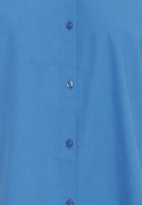 Camicia button-up azzurro chiaro realizzata in tessuto morbido, con sei bottoni rotondi, colletto classico e dettagli di cucitura discreti.