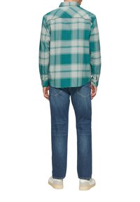 Zielona i szara koszula flanelowa w kratę z kołnierzykiem typu button-down, długimi rękawami i prostym krojem; zestawiona z niebieskimi dżinsami i białymi sneakersami.