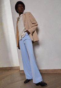 Beige Blazer über einem cremefarbenen Hemd, kombiniert mit hellblauen Schlaghosen und schwarzen Schuhen. Glatter Stoff mit taillierter Passform.