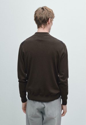 Maglione marrone lavorato a maglia con collo e maniche lunghe, caratterizzato da dettagli a rilievo sulla spalla, abbinato a jeans grigio chiaro.