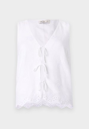 Valge ilma varrukateta tipp, millel on sügav V-kujuline kaelus ja pitsdetail äärtes. Omab esiosas sidumisnõela ja tekstuurset kangast.