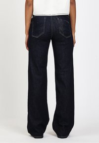 Jeans de pierna ancha en denim oscuro con una textura suave, que presentan bolsillos traseros y pespuntes en contraste. Acabado limpio en el dobladillo.