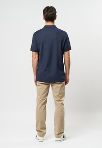 Granatowa koszulka polo z krótkim rękawem i kołnierzykiem oraz spodnie khaki. Strój uzupełniają białe tenisówki z niebieskimi i czerwonymi akcentami.