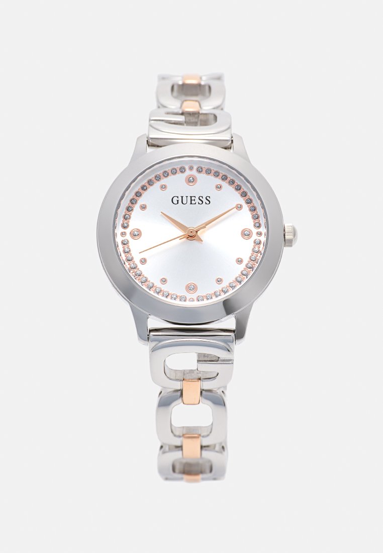Reloj de pulsera Guess en plata y oro rosa con marcadores de hora de cristal y correa metálica enlazada, mostrado sobre un fondo liso.