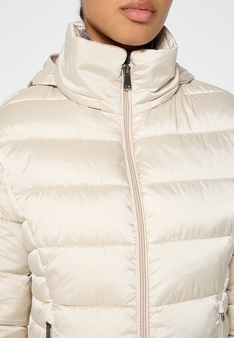 Giacca a vento leggera beige chiaro con colletto alto, design trapuntato, chiusura con cerniera frontale e tasche laterali. Texture del tessuto liscia e lucida.