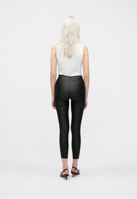 Fekete műbőr leggingsek magas derékkal, testhez álló szabással és sima textúrával. Fehér ujjatlan toppal és fekete magassarkú szandállal viselve.