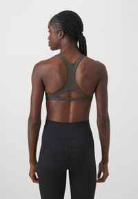 Reggiseno sportivo verde scuro con design a schiena scoperta, caratterizzato da un dettaglio a taglio e una texture liscia. Abbinato a leggings neri a vita alta.