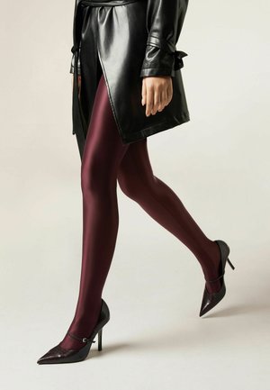 Des collants opaques bordeaux associés à des chaussures à talons hauts noires et texturées. Un manteau en cuir noir avec une ceinture nouée finalise le look.