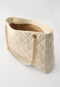 Borsa a tracolla trapuntata beige con catena dorata, texture liscia e tasca interna con zip. Presenta una placca con logo metallico sul davanti.