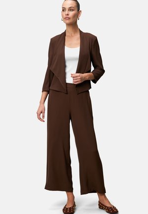 Bruin drapeerlblazer over een witte top, gecombineerd met brede bruine pantalons. Gladde stof, minimalistisch ontwerp en subtiele hardwaredetails.