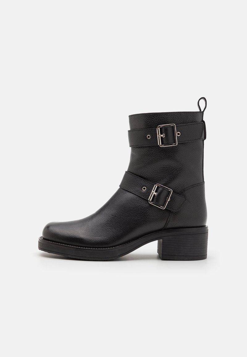 Bottine en cuir noir avec deux boucles argentées, bout arrondi, petit talon bloc et languette à l'arrière.