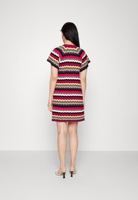 Vestido de manga corta con un patrón de rayas onduladas en colores como rojo, azul marino, blanco y dorado, que presenta un corte holgado y llega hasta la mitad del muslo.