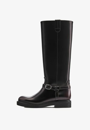 Hoher schwarzer Lederstiefel mit rundem Zehenbereich, niedrigem gestapeltem Absatz und dekorativem Riemen mit silberner Schnalle um den Knöchel.