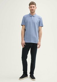 Hele sinine polo särk, millel on tekstuuriga kangas, lühikesed varrukad ja krae, koos slim-fit mustade pükste ja tumedate kingadega.