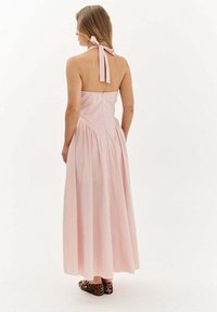 Maxi šaty v svetloružovej tkanine, s holými ramenami a detailom mašle, priliehavá korzetová časť a skládaná sukňa. Na nohách zvierací vzor baleríny.