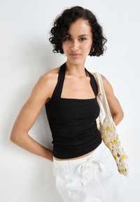 Black halter top with a square neckline, featuring gathered texture. Paired with white drawstring pants and a cream bag with floral accents.