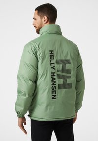 Groene pufferjack met een hoge kraag, elastische manchetten en een zwart logo en graphic print op de achterkant. Gladde, lichte stof.