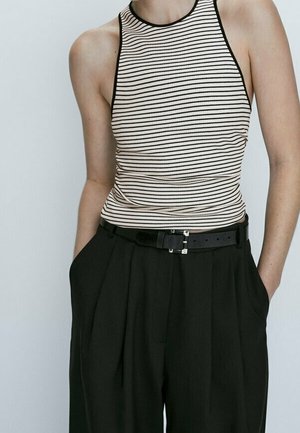 Striped, fitted sleeveless top in beige and black, paired with high-waisted black trousers, featuring pleats and a black belt with a silver buckle.