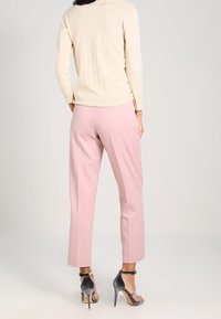 Kremowy sweter i jasnoróżowe spodnie o dopasowanym kroju. Srebrne sandały na wysokim obcasie z paskami wokół kostki. Gładkie tekstury, minimalistyczny styl.