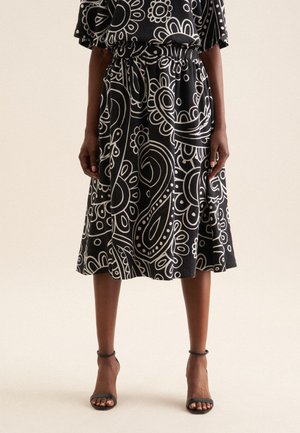 Zwarte rok met witte paisley-patronen, tailleband, uitlopend ontwerp, knie-lengte, gecombineerd met zwarte sandalen met straps.