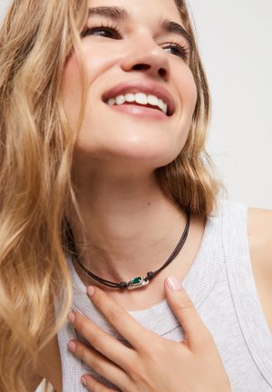 Collier en cuir avec une pierre précieuse verte sertie dans un accent en argent, porté avec un haut gris à texture côtelée.