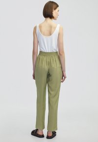 Olivově zelené kalhoty s elastickým pasem a volným střihem, v kombinaci s bílým topem bez rukávů. Hladká textura, rovné nohavice.