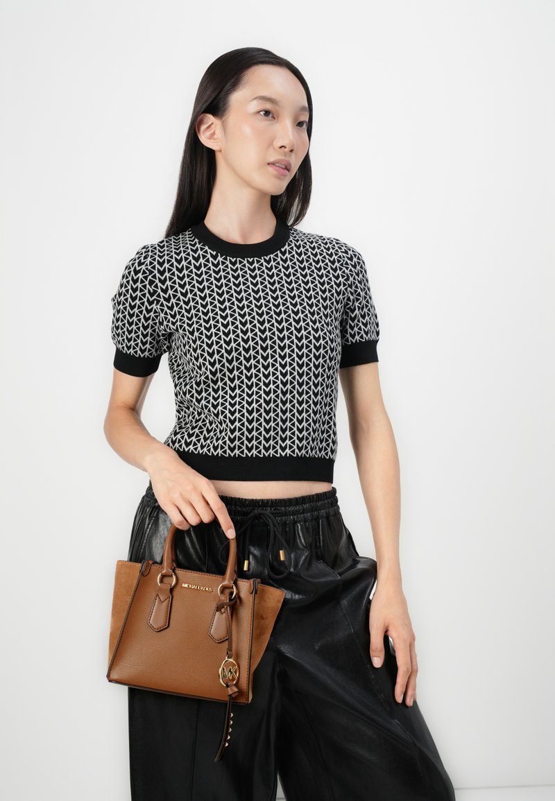 Sac en cuir marron avec des accents texturés et des accessoires en or, associé à un haut à manches courtes noir et blanc à motif et à un pantalon noir.