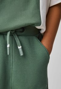 Grønne teksturerede sweatpants med et rillede design, der har en snøre i taljen og et mærkat med teksten "BAKER."