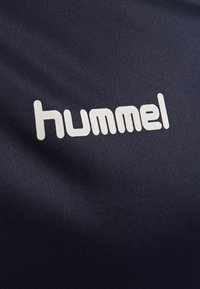 Ciemnoniebieska koszulka sportowa o gładkiej fakturze, z dużym białym logo "hummel" nadrukowanym na przodzie.