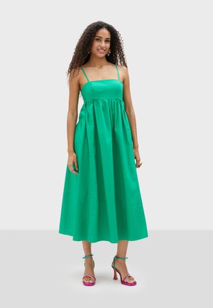 Groene mouwloze jurk met een aansluitend lijfje en een vloeiende rok. Glad stof, gathered taille en minimale hardware details.