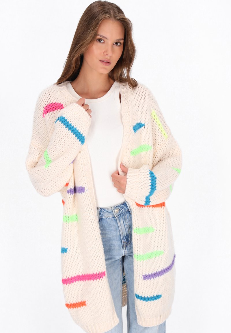 Sweter kardigan w kremowym kolorze z intensywnymi, wielokolorowymi paskami, o luźnym kroju, otwartym przodzie i ściągaczach przy mankietach.