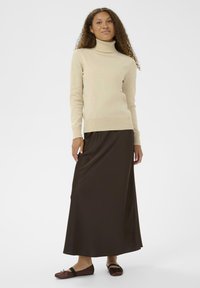 Bežna pletena turtleneck pulover v kombinaciji z dolgo rjavo satenasto krilo in temno rjavimi natikači. Preprost, oprijet dizajn z rebrastimi detajli.