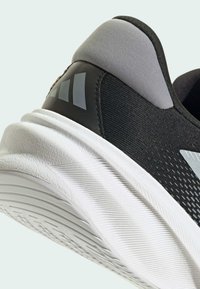 Black athletic shoe with a textured upper, gray padded ankle collar, and a white rubber sole featuring clear treads and branding accents.
