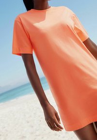 T-Shirt-Kleid mit kurzen Ärmeln und oversized Schnitt in leuchtendem Korall, aus glatter Baumwolle. Verfügt über einen klassischen Rundhalsausschnitt und eine lockere Passform.