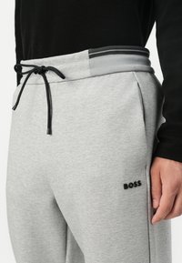 Grå joggebukser med elastisk midje og svarte og grå striper, snor, og en liten svart "BOSS" logo på siden.
