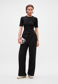 Juodas ribotas trumpų rankovių marškinėliai, derinami su aukšto liemens juodomis kelnėmis su subtiliu spindinčiu tekstūru, laikanti sidabrinę rankinę. Sidabriniai batai.