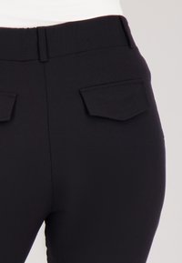 Zwarte broek met een gladde textuur, voorzien van een middelhoge taille, subtiele stiksels en twee achterzakken met puntige kleppen.