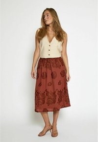 Top beige senza maniche con bottoni abbinato a una gonna midi ricamata floreale marrone. Tessuto morbido e leggero.