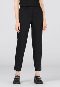 Svarta skräddarsydda byxor med en slät textur, avsmalnande ben, bälteshällor och sidofickor. Matchas med svarta loafers som har en guldkedja som accent.