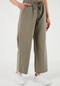 Licht olijfgroene, wijde broek met een elastische tailleband en trekkoord, voorzien van zijzakken en opgerolde manchetten, gecombineerd met witte sneakers.