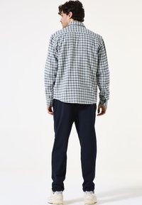 Geverfd langsluiter shirt in blauw, wit en groen met knoopmanchetten, gecombineerd met marineblauwe joggers en lichte sneakers.